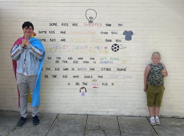 A boy and a teenager standing outside a wall with writing on it