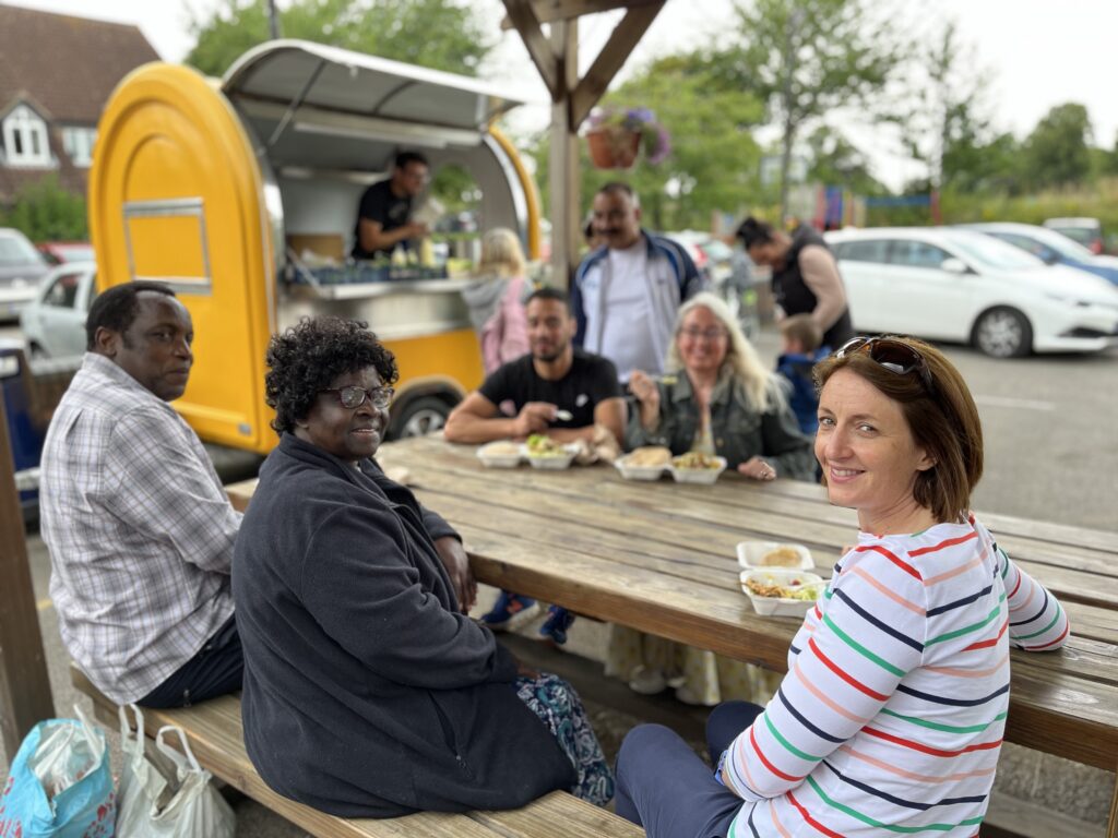 people sitting around sharing lunch outside on a wooden table with a yellow food truck behind them