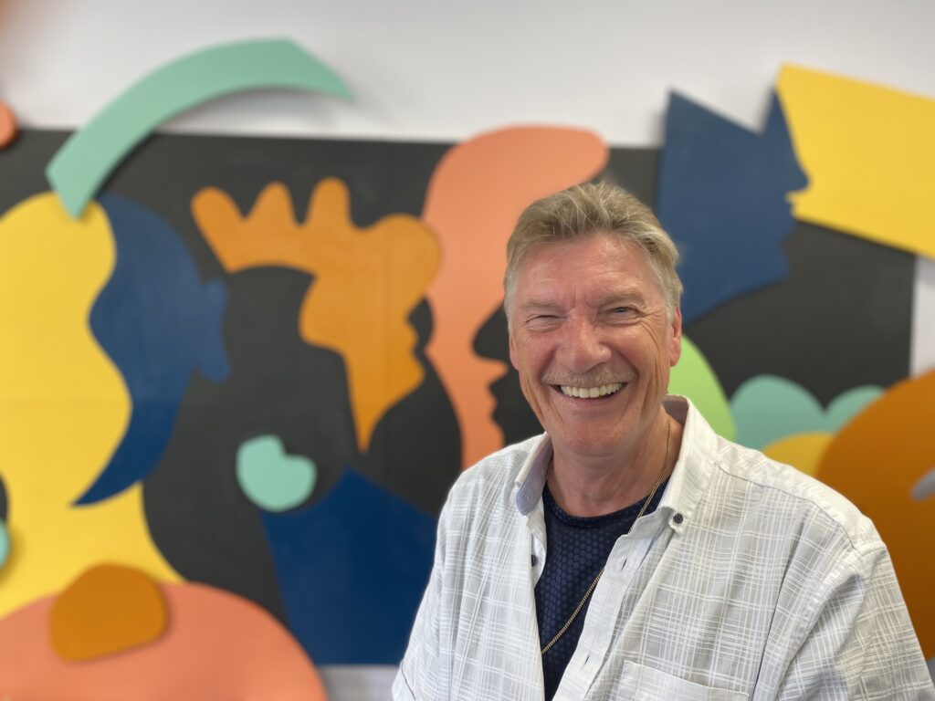 A man smiling in front of a colourful background