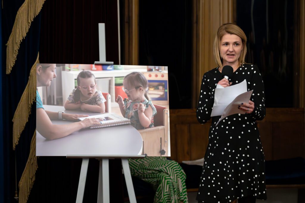 woman presenting next two a photo of two young girls with down's syndrome